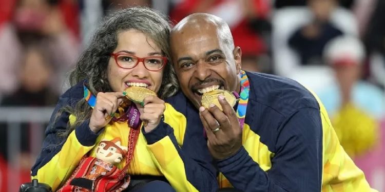 O calheiro Roberto Ferreira ao lado da atleta Evelyn Oliveira, da bocha. De costas para o jogo, ele ajusta a calha para os lançamentos da parceira. Foto: Daniel Zappe/EXEMPLUS/CPB O calheiro Roberto Ferreira ao lado da atleta Evelyn Oliveira, da bocha. De costas para o jogo, ele ajusta a calha para os lançamentos da parceira. Foto: Daniel Zappe/EXEMPLUS/CPB