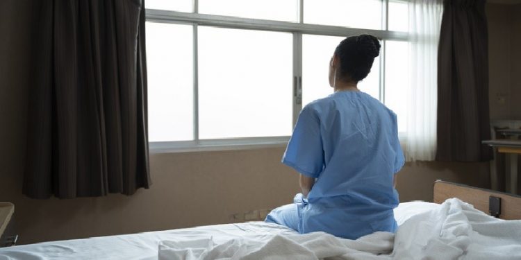 Mulher sentada em cama de hospital olhando pela janela Mulher sentada em cama de hospital olhando pela janela