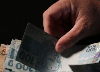 Registro de uma mão segurando algumas cédulas de reais com notas de 100 e 50. Foto: José Cruz/Agência Brasil